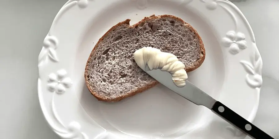 Butter spreader knife with butter on bread placed on plate, small kitchen utensil useful for visualizing length close to inches