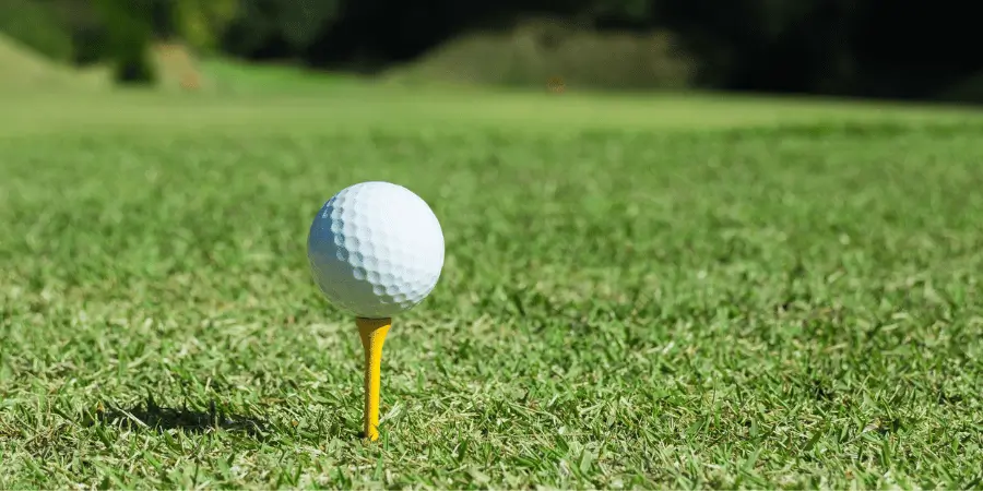 Golf ball placed on yellow tee on grass field, close-up outdoor sports scene with blurred background