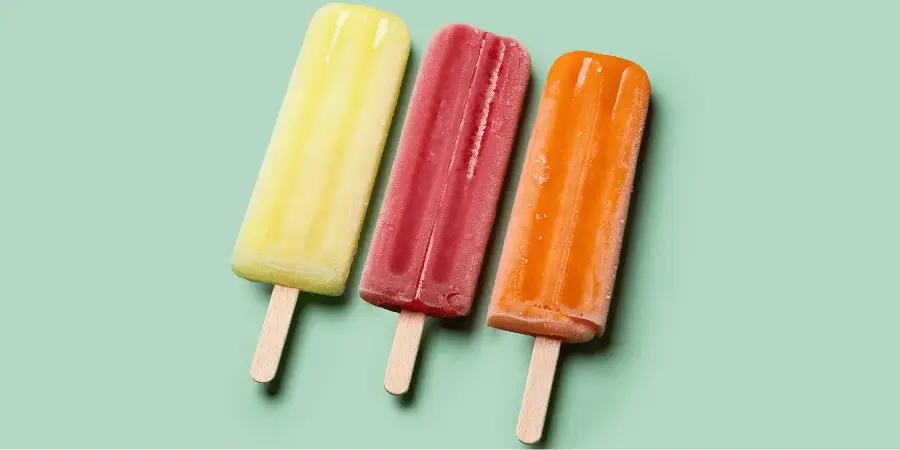 Three colorful popsicles on sticks arranged on green background, frozen dessert with vibrant tones and texture