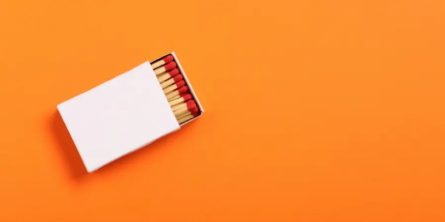 Open matchbox showing wooden matches with red tips on an orange background, minimal composition with copy space