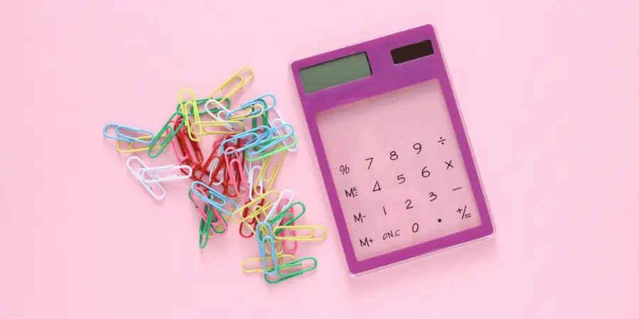 Colorful paper clips scattered beside a pink calculator on a pastel background, office supplies flat lay composition