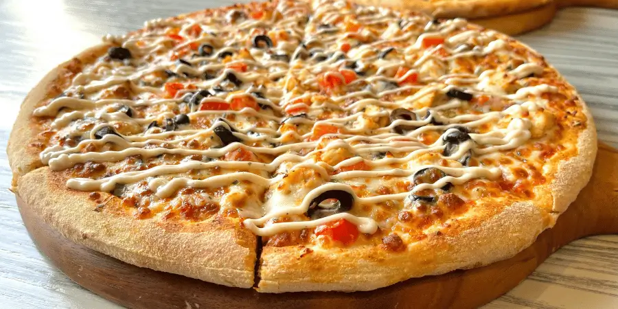 Whole round pizza with toppings and sauce placed on a wooden board on table surface