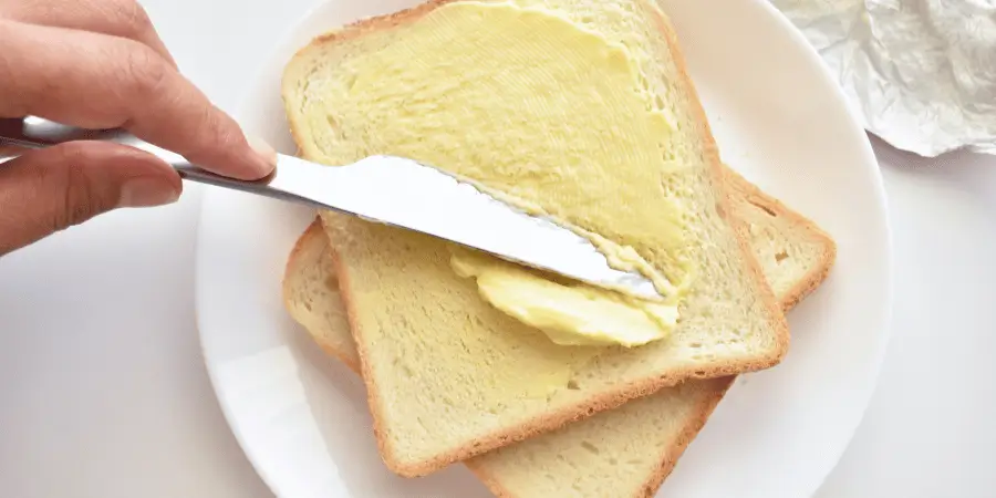 Butter knife spreading butter on toasted bread during breakfast preparation in a home kitchen